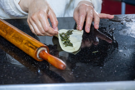 preparing arabic traditional pastries by female hands stuffing them with spinach and red chiliの写真素材