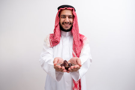 arabic man holding dates represents hospitality and generosity wearing kandura with keffiyeh on isolated white background for eid celebrationsの写真素材