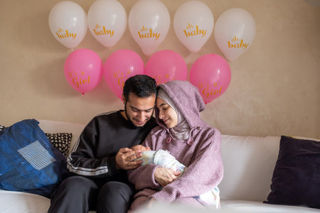 Arabic muslim couples holding their newborn baby celebration in living room with balloons and pink