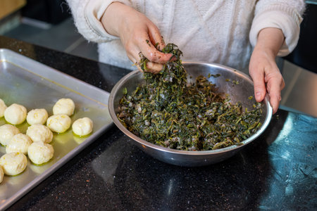 preparing traditional pastries by female hands stuffing them with spinach and red chiliの写真素材