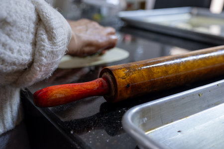 old woman hands using rolling pin to flatten the dough on black marble