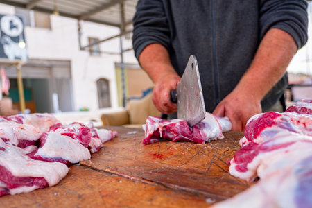 A man with a focused expression carefully slices through a piece of meat on a sturdy wooden cutting board. Each deliberate motion of his knife reflects years of practiced skillの写真素材