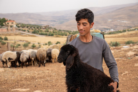 young arabian male holding black sheep in his hand with cheerful look on his face feeling happy in eid al adhaの写真素材