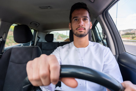 A cheerful young man with a beard, wearing a traditional Middle-Eastern outfit, smiles confidently while seated in his car. He appears to be enjoying a drive through a scenic countrysideの写真素材