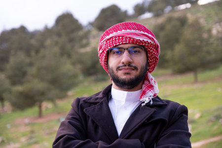 An Arab man in nature clears his mind and thinks positively about the future, surrounded by trees and clouds wearing a jacket due to change in climateの写真素材