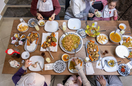 A Muslim family gathers around a rectangular table, sharing a heartwarming meal together, with members of various ages adding to the warmth and joy of the occasionの写真素材