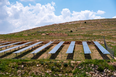 A solar farm is built on a hill under a cloudy sky, surrounded by nature, creating an...
