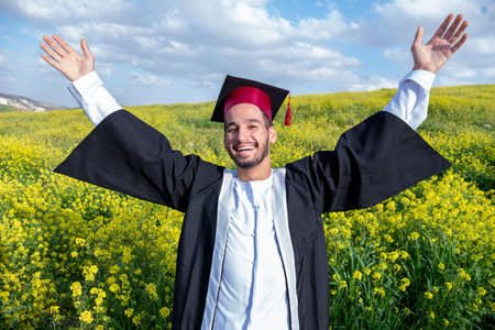 Cheerful young arab male celebrating his graduation in a beautiful yellow flowers field with smile...