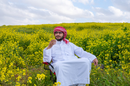 An Arab person enjoys a spring picnic in a meadow near Abu Dhabi. Seated on chairs, they savor cups of coffee under a blue sky with scattered cloudsの写真素材