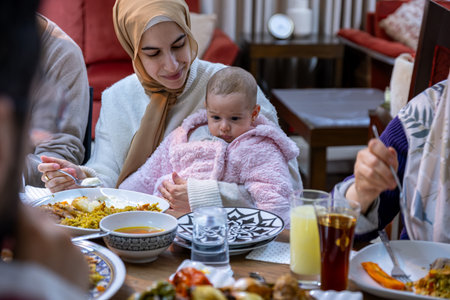 A tender portrait captures a mother seated at the family table, lovingly caring for her baby while they share a meal together. The bond between them shines through as they create cherished memories in the heart of their homeの写真素材