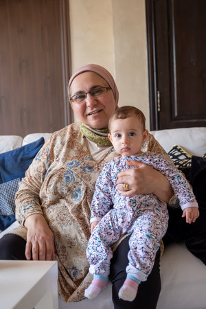 In the cozy living room, a grandmother joyfully holds her granddaughter, both radiating excitement...
