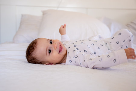 Smiling baby in star patterned pajamas lying on a white bed