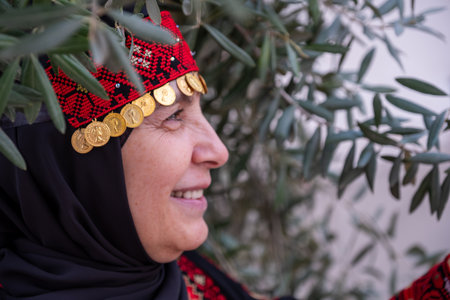 Portrait Of woman wearing palestinian traditional clothes in olive trees field holding branch in her hand with smile on her faceの写真素材