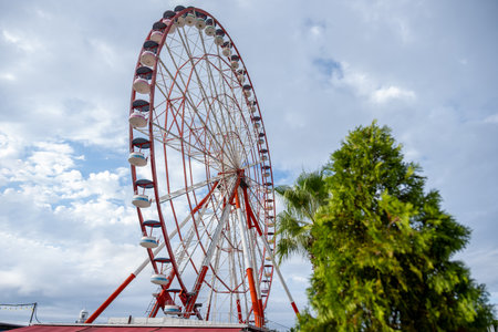 Red and White Ferris Wheel Against Blue and Cloudy Sky with Copy Spaceの写真素材