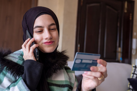 muslim Woman wearing hijab using phone to contact customer care about her bank card issue