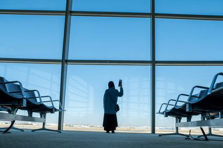 Female holding her passport behind airport waiting seats and in front of windowsの写真素材
