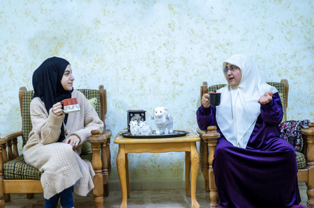 young female with her mother having coffee together indoors while chatting and smiling togetherの写真素材