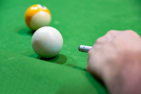 Young adult bearded male playing billiards with his friends focusing on white ball to hit it with...