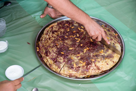 Man hands cutting musakhan bread with knife for guests and family to eat together