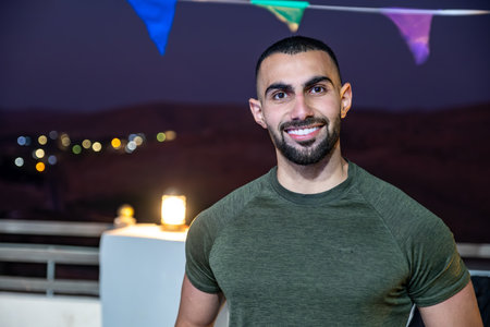 Young arabian adult with fit muscular body with elegant and confident expression on his face during night with blurred lights in backgroundの写真素材