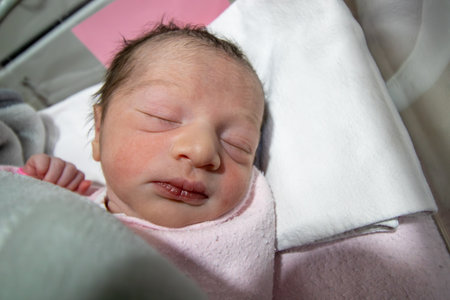 On her first day of life, a newborn baby girl wears a pink hospital ID bracelet on her hand