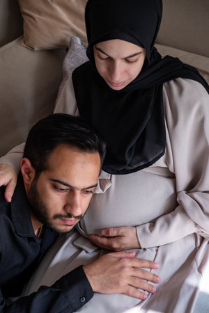 Arabian man is listening to his beautiful pregnant wife's tummy and smilingの写真素材