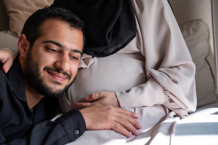 Arabian man is listening to his beautiful pregnant wife's tummy and smiling