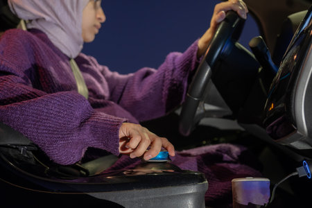 Pregnant arabic muslim woman driving car at night wearing winter clothes ,hijab and seat belt driving in confidently and feeling safeの写真素材