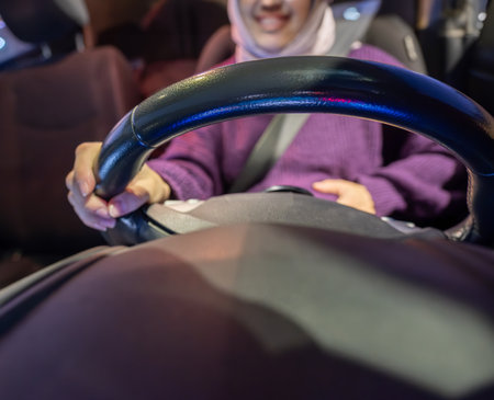 Pregnant arabic muslim woman driving car at night wearing winter clothes ,hijab and seat belt driving in confidently and feeling safeの写真素材
