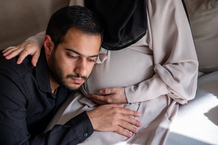 Arabian man is listening to his beautiful pregnant wife's tummy and smilingの写真素材