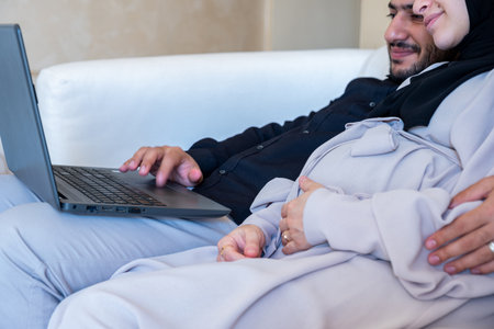 male and pregnant female chatting about pregnancy and how to rise child while using laptop in home...