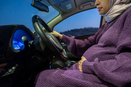 Pregnant arabic muslim woman driving car at night wearing winter clothes ,hijab and seat belt...