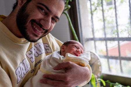 Father holding his newborn son with cheerful reaction and smile on his baby face