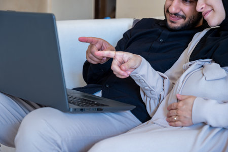 male and pregnant female chatting about pregnancy and how to rise child while using laptop  in home...