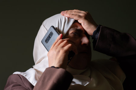 A Muslim woman was informed by phone call of shocking news or misfortune, and her expression shows...