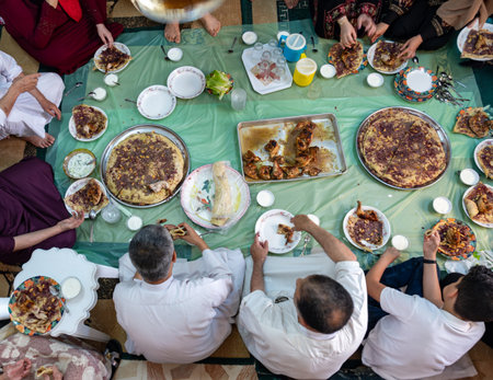 Family and friends gathering together at home for eating musakhan and chicken,sitting on floor in arabian traditional way of eatingの写真素材