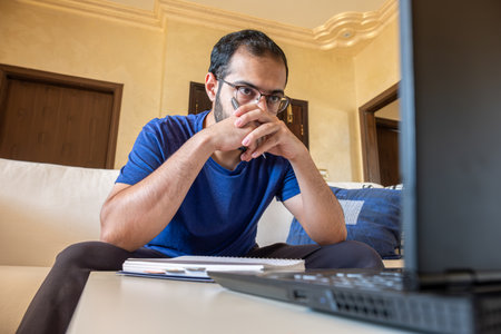 Young arabic man working at home with laptop and papers on desk