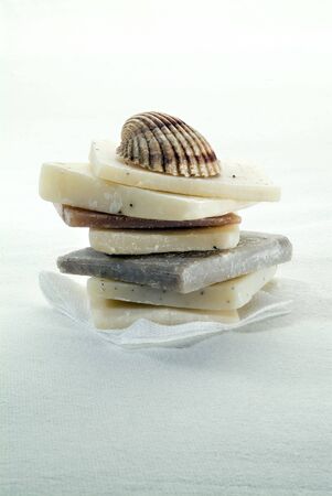 pile of hand made natural colors soaps on white cloth with a shellの写真素材