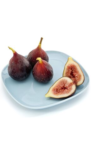 three whole figs and one sliced one on a square blue plateの写真素材