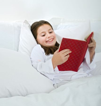 young girl lying in bed and reading a red bookの写真素材