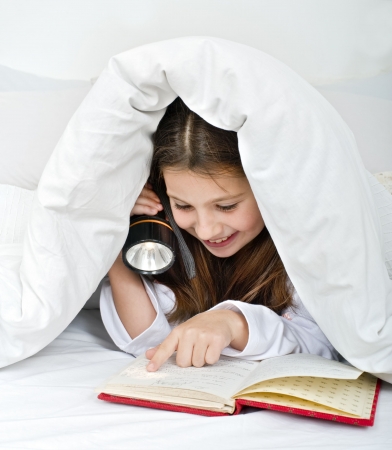 girl reading under blanket with flashlightの写真素材