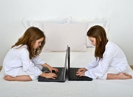 two girls with laptop computers on the bed