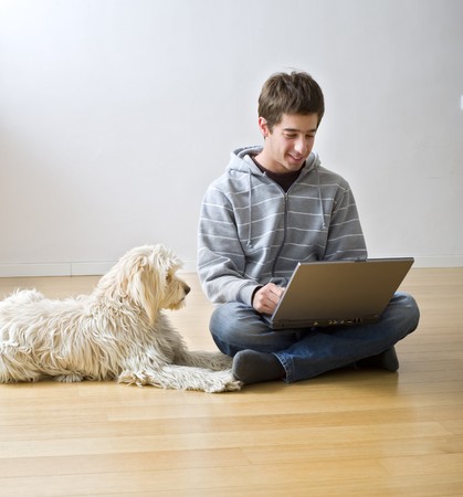 teenager with a laptop computer and his dog on a parquet floorの写真素材