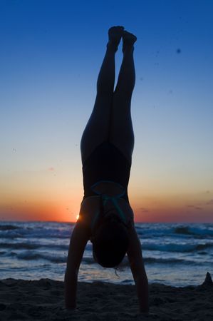young girl's silhouette handstanding on the beach at sunsetの写真素材