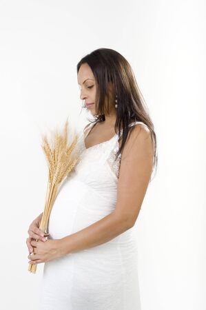 Pregnant woman with a sheaf of wheat and white dress isolated on whiteの写真素材
