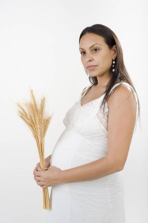 Pregnant woman with a sheaf of wheat and white dress isolated on whiteの写真素材