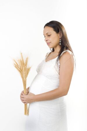 Pregnant woman with a sheaf of wheat and white dress isolated on whiteの写真素材