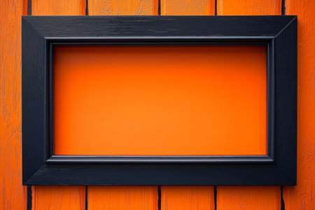 A black picture frame is centered on an orange painted wooden background providing a blank space for text or images.の素材