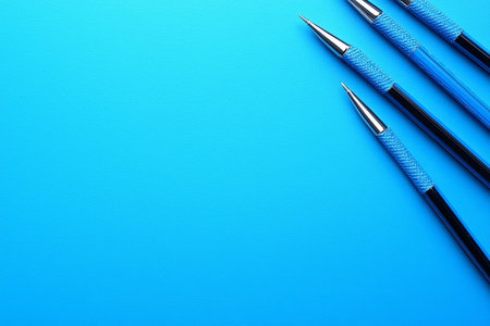 Three stylish blue pens are arranged on a bright blue textured background, creating a clean and minimalist composition.の素材