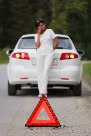 Woman calls to a service standing by a white car. Focus is on the red triangle sign 